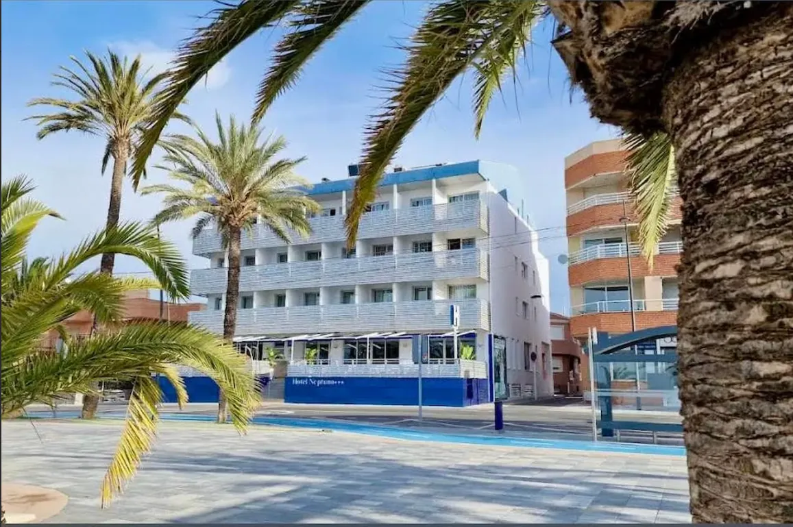 Façade of Hotel Neptuno among palm trees on a sunny seafront promenade